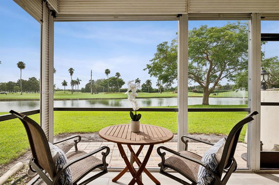 Patio view looking out to a lush green lawn and small lake with trees in the background.