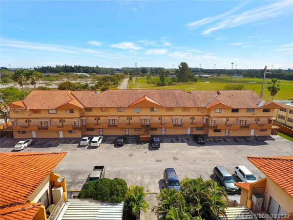 Front view of a two-story building with red tiled roof and parking area in front.