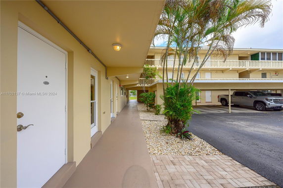 Outdoor parking area adjacent to a multi-story building with covered parking spaces and surrounding plants.