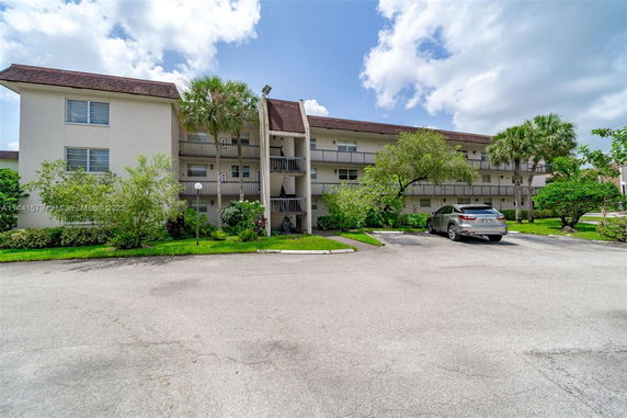 Front view of a three-story apartment building with balconies and a parking area.