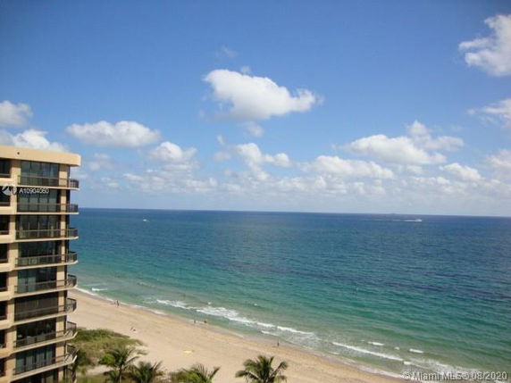 View from building overlooking a sandy beach and ocean with a blue sky.