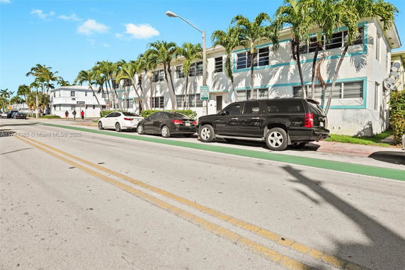 Front view of a two-story building with palm trees and parked cars on the street.