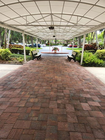 Covered walkway leading to an outdoor parking area with benches and plants.