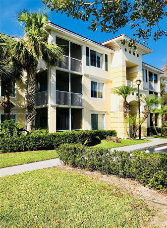 Front view of a three-story apartment building with balconies and palm trees.