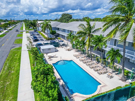 Outdoor view of a swimming pool surrounded by lounge chairs and palm trees adjacent to a building.