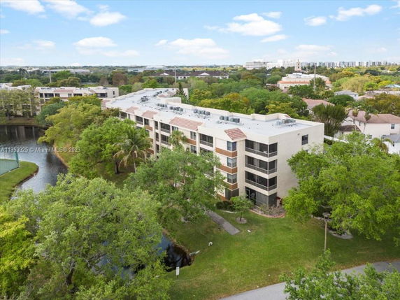 Aerial view of a multi-story residential building surrounded by trees and a small body of water.