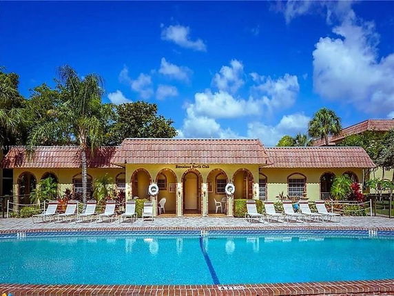Outdoor swimming pool in front of a building with arches and tiled roof.