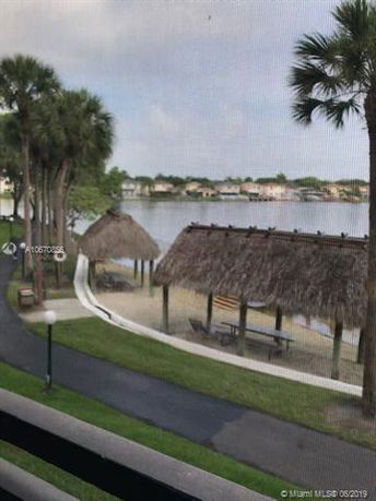View from a building showing a lakeside area with palm trees and thatched roof structures.