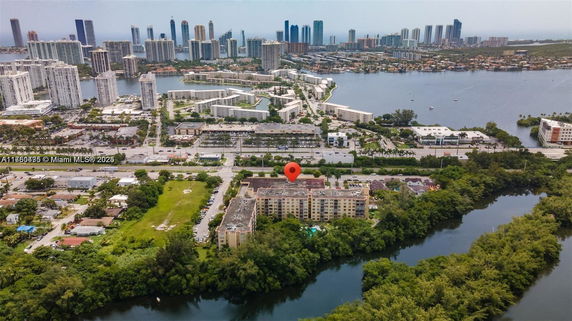 Aerial view of an urban area with residential and commercial buildings, nearby waterways, and skyscrapers in the background.