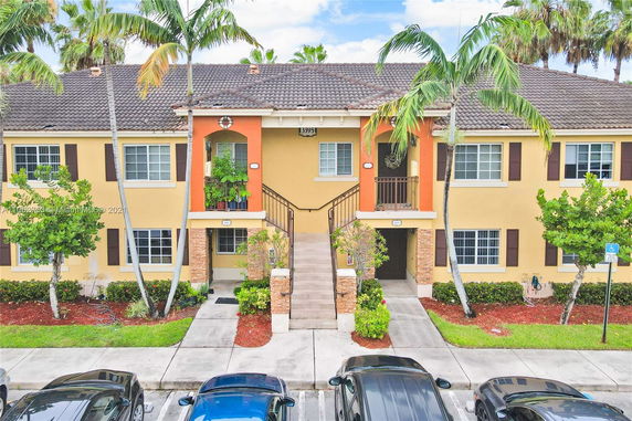 Front view of a two-story residential building with a central staircase and tropical landscaping.