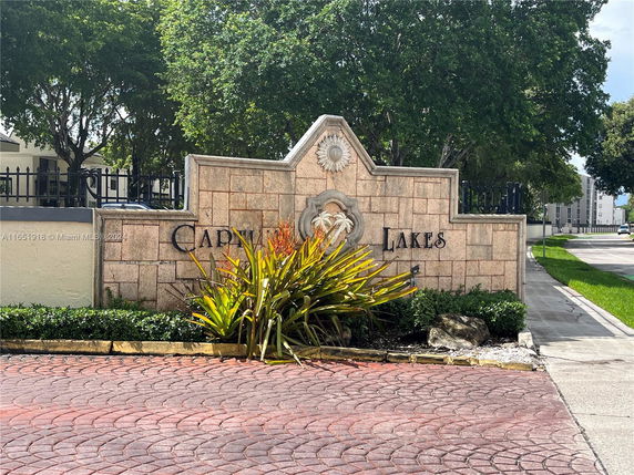 Stone entrance sign for a residential area with trees and pavement.