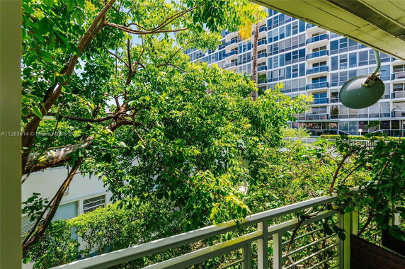 Balcony view of a tall residential building partly obscured by leafy trees.