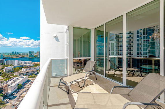 Balcony view from a high-rise building with large glass doors and lounge chairs.
