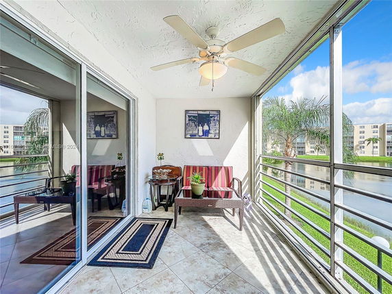 Enclosed balcony with seating area overlooking a landscaped area with palm trees.