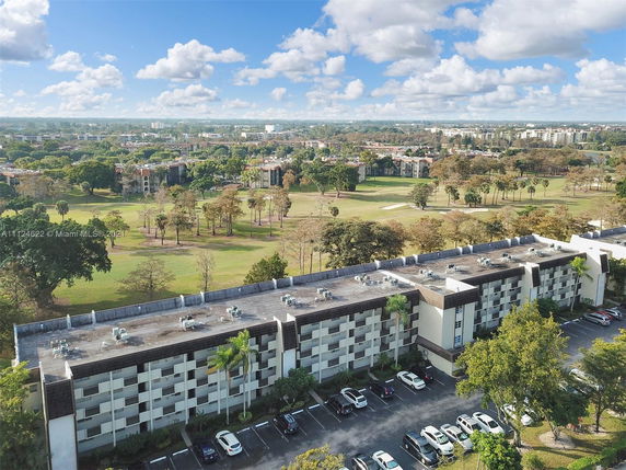 Aerial view of a building with a flat rooftop and surrounding landscape, including trees and open fields.