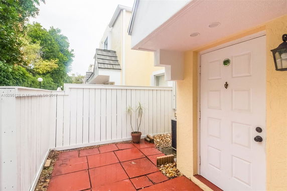View of the entrance area with a white door, patio, and white fenced surroundings.