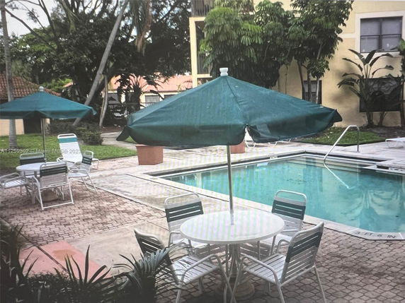 Outdoor swimming pool area with tables, chairs, and umbrellas.