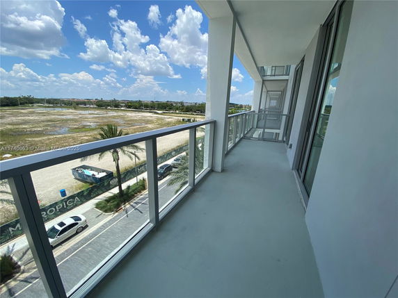 View from a balcony with glass railing overlooking an open area and a road below.