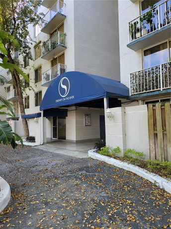Front view of a multi-story residential building with balconies and a blue canopy entrance.