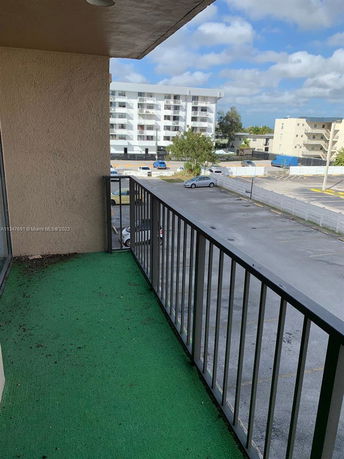 View from a balcony towards a parking area and neighboring buildings.
