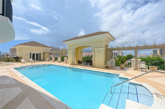 Outdoor swimming pool with surrounding lounge chairs and pergola.