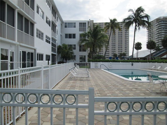 Outdoor swimming pool area with surrounding buildings and palm trees.