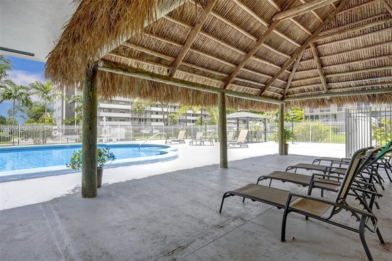 View from under a thatched pavilion showing a swimming pool and buildings in the background.