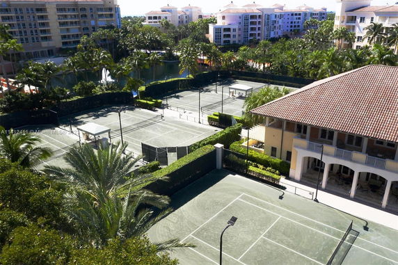 View of multiple tennis courts surrounded by buildings and palm trees.