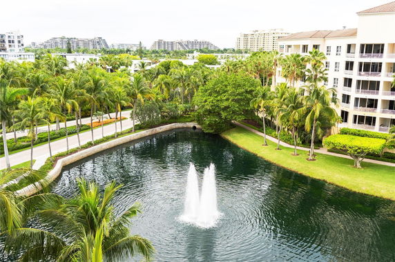 View of a building surrounded by palm trees and a large pond with fountains.