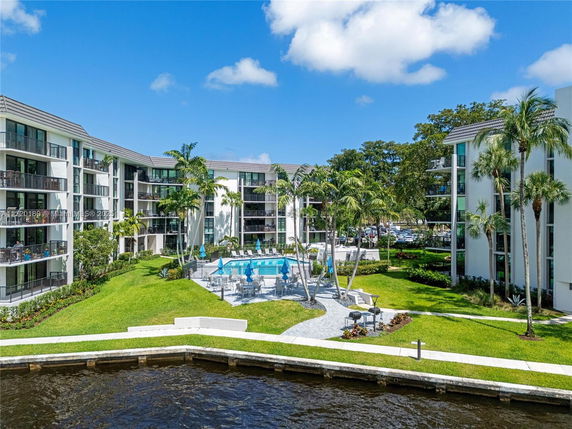 View of an apartment complex with balconies facing a grassy area and a pool.