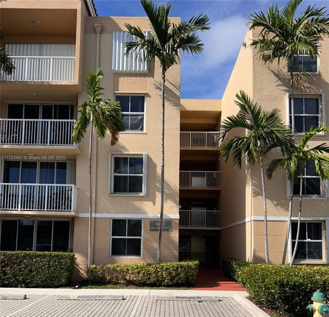Front view of a multi-story apartment building with balconies and palm trees.