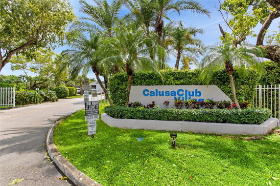 Entrance area with signage for Calusa Club Village surrounded by greenery.