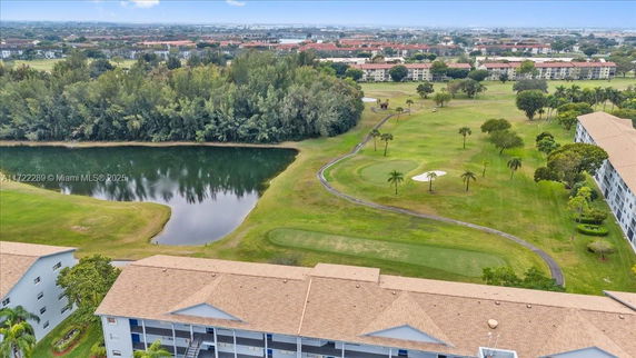 Aerial view overlooking a green golf course with a pond and trees, surrounded by residential buildings.