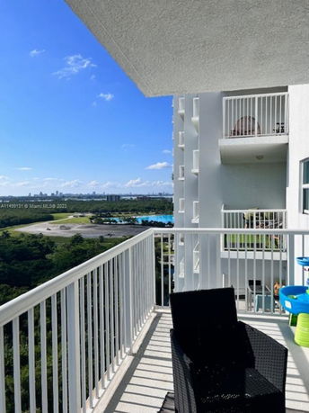 Balcony view from a high-rise building overlooking greenery and distant cityscape.