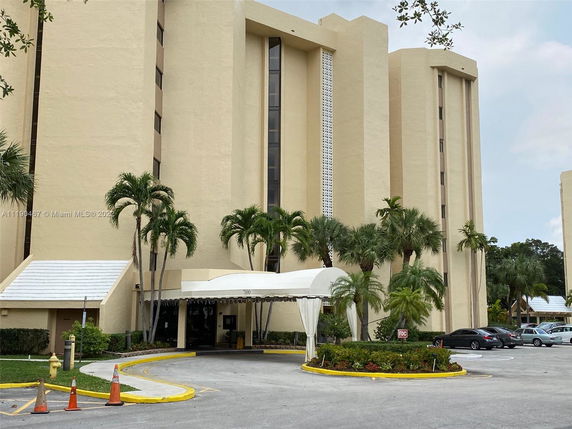 Front view of a multi-story building with a covered entrance and surrounding palm trees.