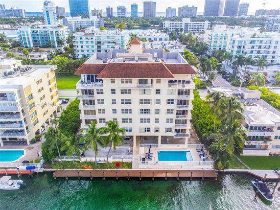 Panoramic view of a multi-story waterfront apartment building with a swimming pool and surrounding cityscape.