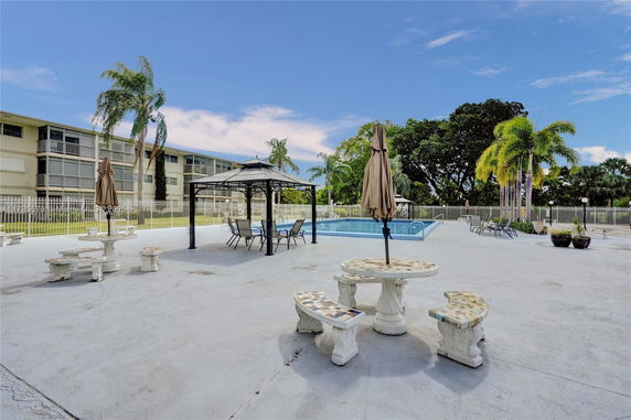 Outdoor area with a swimming pool, tables, and chairs under umbrellas.