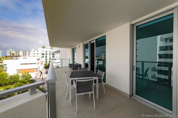 View from a modern balcony with glass railings and outdoor furniture, overlooking adjacent buildings.