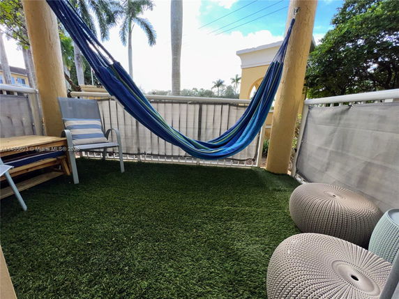 Outdoor balcony area with artificial grass, a blue hammock, and outdoor seating.