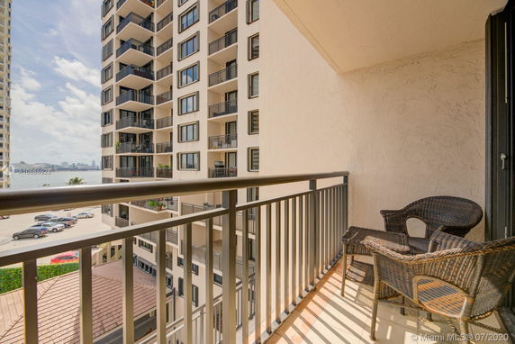 Balcony view of a tall apartment building with multiple floors and balconies, overlooking a parking area and water in the background.