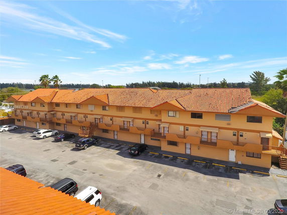 View of a multi-story building with tiled roofs and a parking area in front.