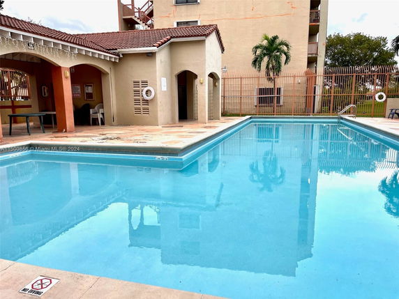Outdoor swimming pool area with a small building and palm tree.