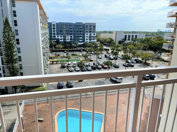View from a balcony overlooking a pool and parking area with high-rise buildings in the background.