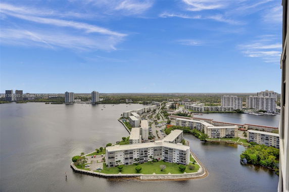 Aerial view of waterfront buildings with a river and distant cityscape.