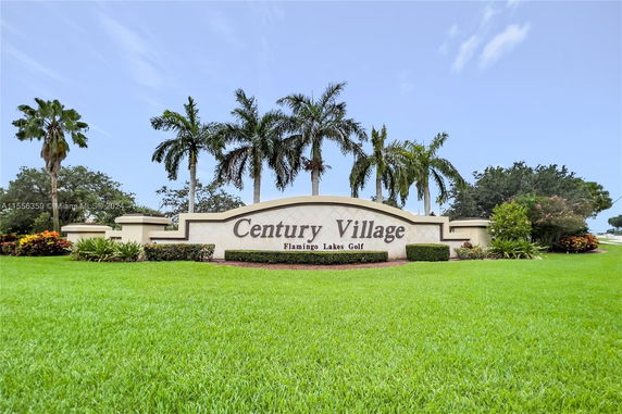 Sign for Century Village Flamingo Lakes Golf with palm trees and landscaped greenery.