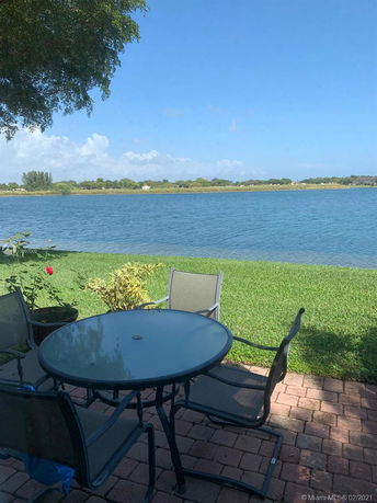 Outdoor view of a lake with a patio area and outdoor furniture in the foreground.