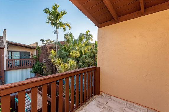 Balcony view with nearby buildings and tropical plants visible.