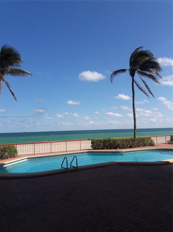 Outdoor swimming pool near a beach with palm trees.