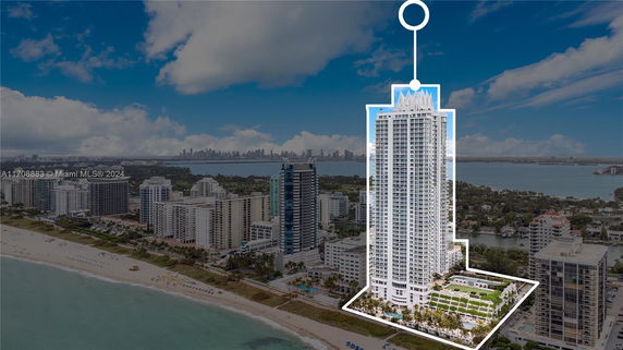Aerial view of a tall, modern skyscraper highlighted along a coastline, surrounded by other high-rise buildings and a beach.