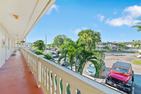 Balcony view overlooking parked cars and surrounding green area.